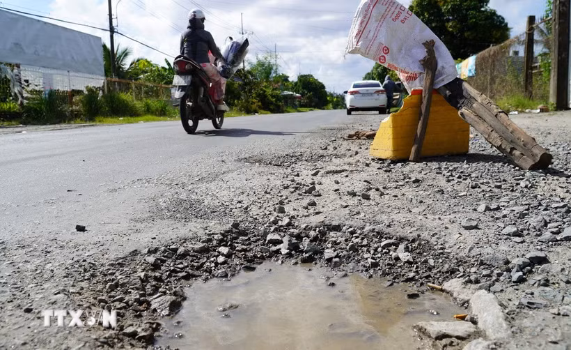 Người dân đặt vật dụng cảnh báo người lái xe né tránh các ổ gà, ổ voi trên quốc lộ 80. (Ảnh: Văn Sĩ/TTXVN)