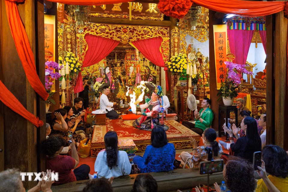 Toàn cảnh không gian thực hành nghi lễ hầu đồng tại đình Đông Thành, với thanh đồng thực hiện các động tác diễn xướng trước ban thờ, bên cạnh những người phụ lễ và đông đảo người dân tham dự. (Ảnh: Phạm Tuấn Anh/TTXVN)