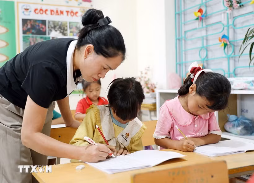 Giáo viên Trường Phổ thông Dân tộc Bán trú Tiểu học và Trung học cơ sở Thu Lũm hướng dẫn học sinh lớp 1 tập viết chữ. (Ảnh: Quý Trung/TTXVN)
