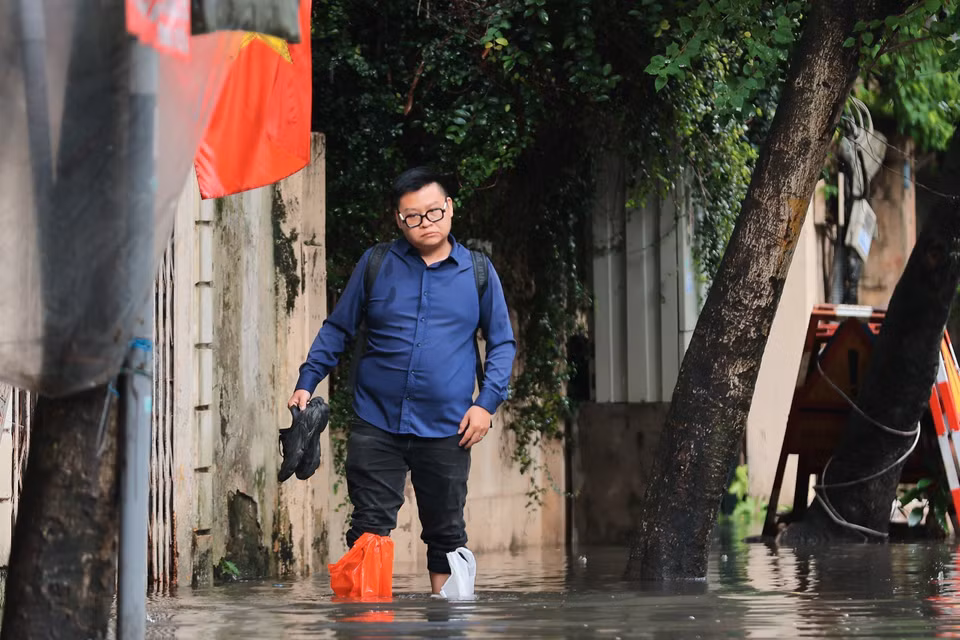 Nhiều người phải lội ra khỏi nhà để đến cơ quan vì không còn đường nào khác hay không thể chờ đến khi nước rút. (Ảnh: Hoàng Hiếu/TTXVN)
