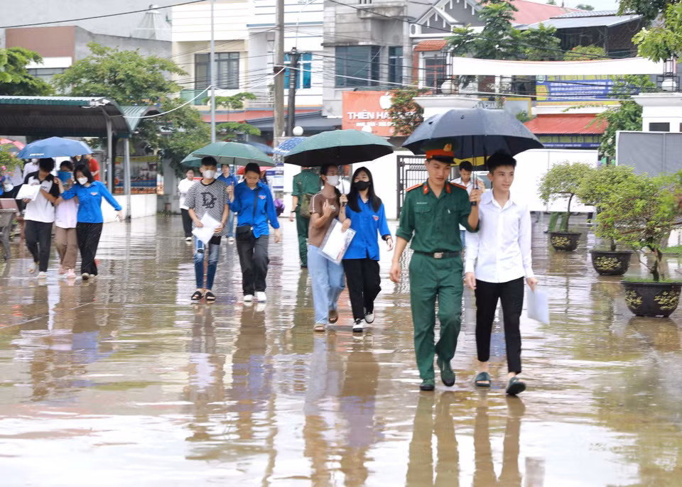 Các thí sinh được lực lượng Bộ đội và thanh niên tình nguyện che ô tại điểm thi Trường THPT Trần Hưng Đạo, huyện Tam Dương, tỉnh Vĩnh Phúc. (Ảnh: Hoàng Hùng/TTXVN)