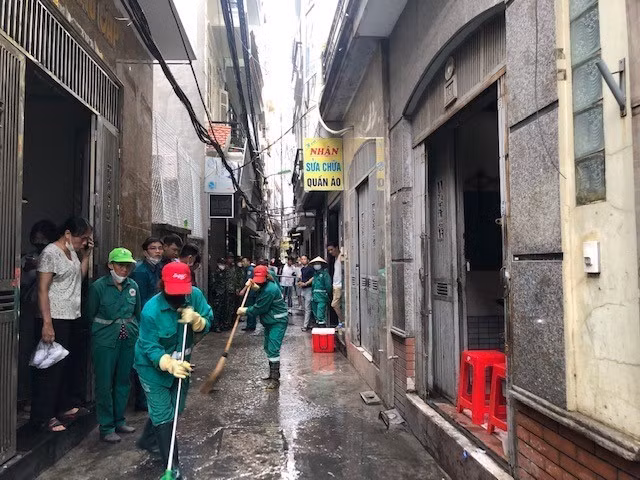 Lực lượng chức năng quận Thanh Xuân dọn dẹp vệ sinh trước chung cư mi ni xảy ra vụ cháy khiến nhiều người thương vong trên phố Khương Hạ. (Ảnh: TTXVN phát)