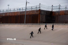Những người di cư chuẩn bị vượt qua bức tường biên giới Mỹ-Mexico. (Ảnh: THX/TTXVN)