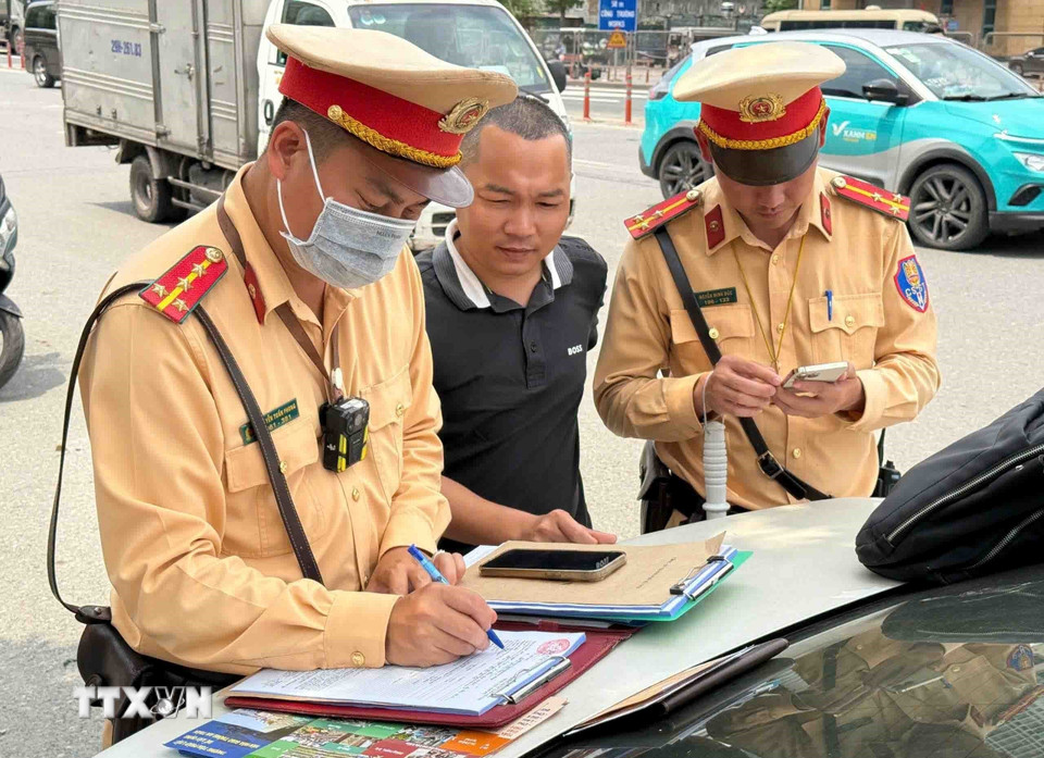 Cán bộ, chiến sỹ đội CSGT số 6 lập biên bản xử phạt lỗi dừng, đón trả khách sai quy định với tài xế xe khách. (Ảnh: Phạm Kiên/TTXVN)