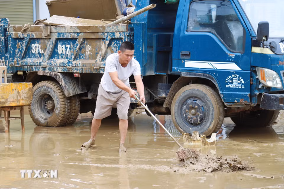 Người dân dọn bùn đất trước nhà ở. (Ảnh: Xuân Tiến/TTXVN)