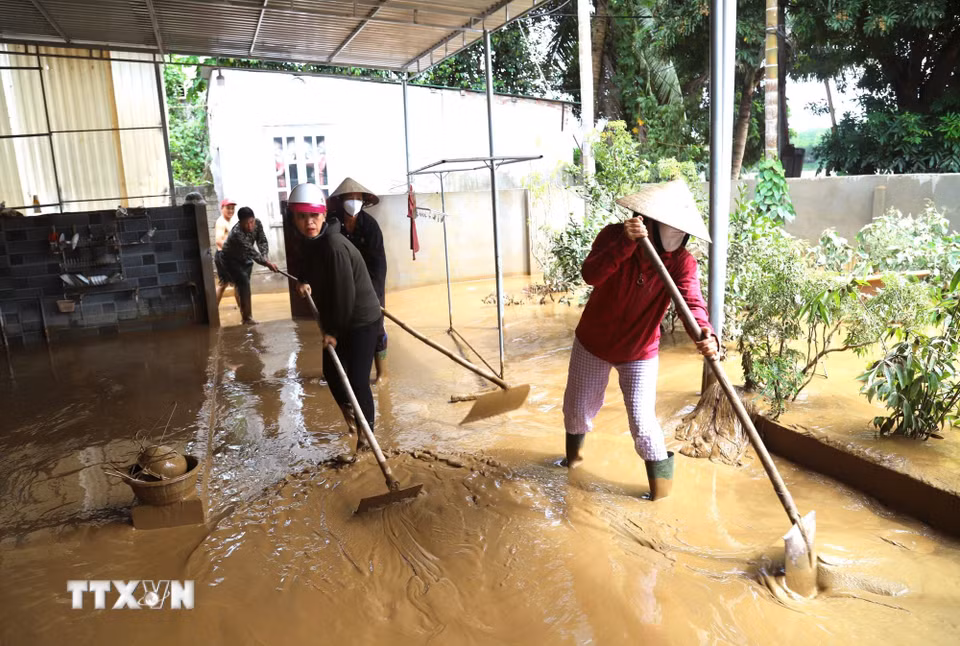 Người dân hỗ trợ, giúp nhau đẩy hàng khối bùn, đất bẩn ra khỏi sân nhà. (Ảnh: Xuân Tiến/TTXVN)