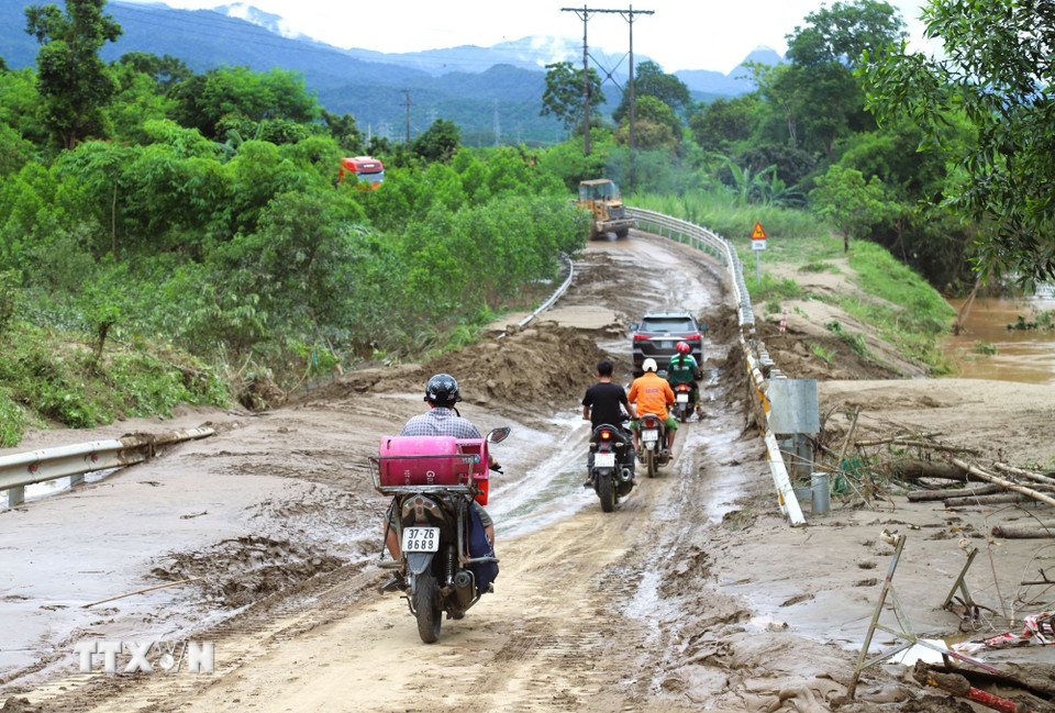 Người dân điều khiển phương tiện ôtô, xe máy di chuyển qua một điểm ngập trên quốc lộ 7 vừa thông tuyến tạm thời vào trưa ngày 24/7. (Ảnh: Xuân Tiến/TTXVN)