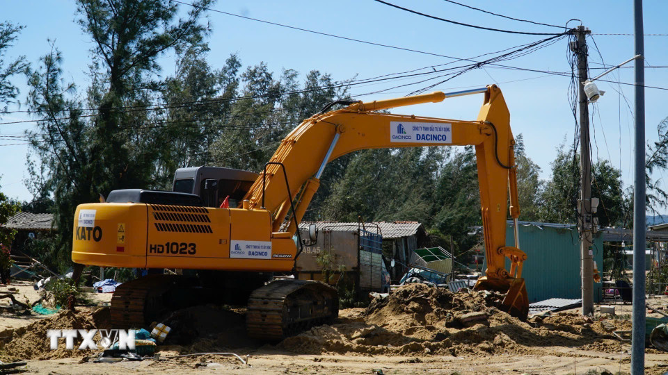 Người dân sử dụng cần cẩu để múc cát cứu tài sản bị cát vùi lấp. (Ảnh: Sỹ Thắng/TTXVN)