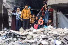 Người dân Palestine đứng trên đống đổ nát của những tòa nhà bị phá hủy sau các cuộc không kích của Israel xuống Dải Gaza. (Ảnh: THX/TTXVN)