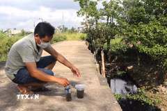 Người dân lấy nước từ kênh Chìm cho vào chai để thấy rõ màu đen. (Ảnh: Đinh Hương/TTXVN)