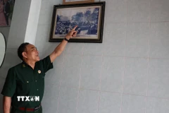 Cựu chiến binh Trần Dân bên bức hình chụp cùng đồng đội tại Dinh Độc Lập vào 13h30 ngày 30/4/1975. (Ảnh: Hoàng Ngà/TTXVN)