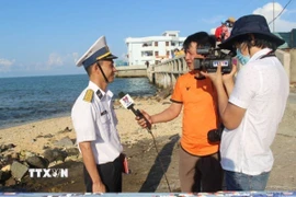 Các phóng viên Thắng Trung (cầm mic) và Sỹ Tuyên (TTXVN) quay phỏng vấn cán bộ hải quân trực tiếp làm nhiệm vụ canh gác bảo vệ trên đảo Đá Thị, Trường Sa hồi tháng 4/2021. (Ảnh: Phan Sáu/TTXVN)