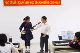 Giáo viên hướng dẫn học sinh sử dụng nhạc cụ dân tộc. (Ảnh: Phan Quân/TTXVN)