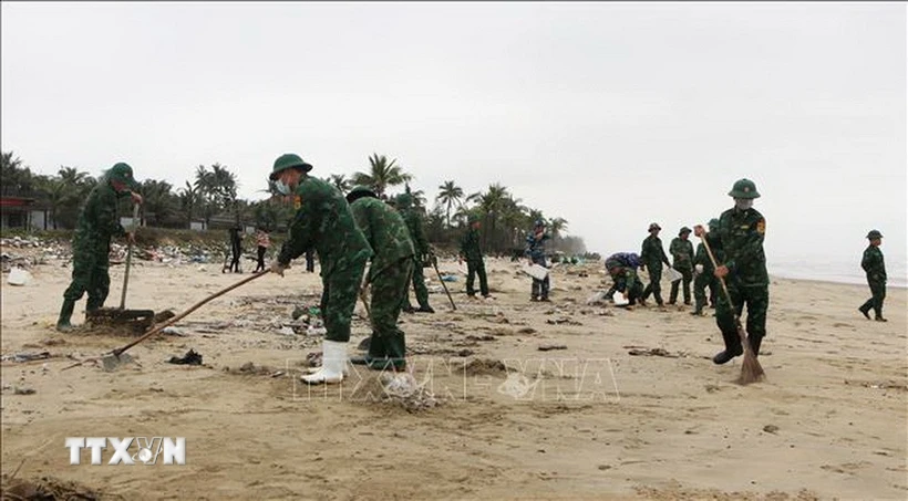 Các lực lượng khẩn trương thu gom dầu tràn vón cục trôi dạt vào bờ biển huyện Phú Lộc. (Ảnh: Tường Vi/TTXVN)