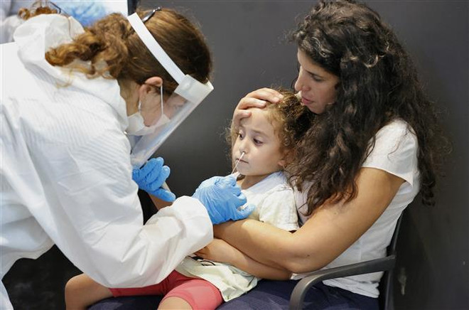 Nhân viên y tế lấy mẫu xét nghiệm COVID-19 cho trẻ em tại Tel Aviv, Israel. (Ảnh: AFP/TTXVN) Mô hình chống dịch COVID-19 của Israel trước làn sóng Omicron ảnh 2