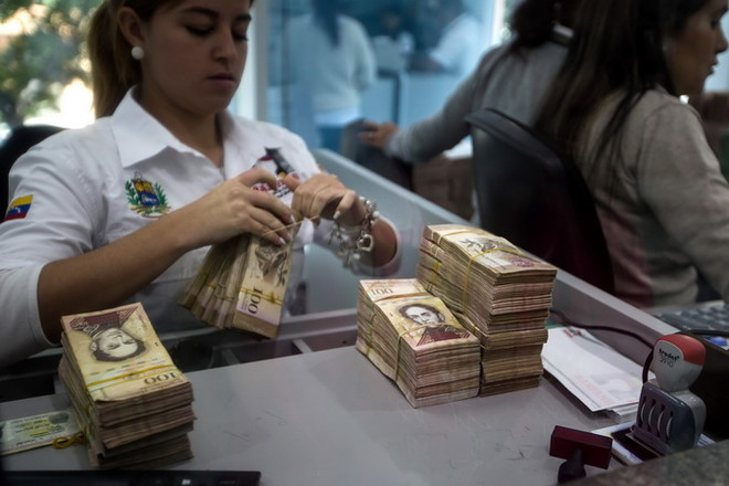 Kiểm tiền mệnh giá 100 Bolivar tại ngân hàng ở Caracas ngày 13/12. (Nguồn: EPA/TTXVN) Venezuela: Nhiều đối tượng kích động bạo lực trong thời gian đổi tiền ảnh 1