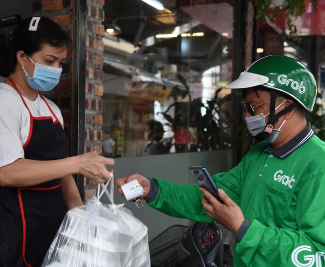 Một shipper làm việc cho Grab lấy đồ ăn tại cửa hàng ở Hà Nội. (Nguồn: AFP) Đà tuột dốc của cổ phiếu Grab khiến Singapore 'thức tỉnh' ảnh 2