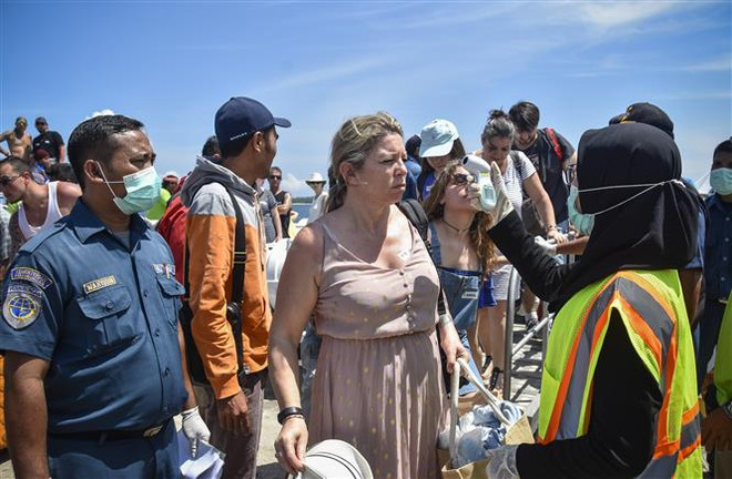 Nhân viên y tế kiểm tra thân nhiệt của du khách nước ngoài tại cảng Bangsal trên đảo Pemenang Lombok, Indonesia, nhằm ngăn chặn khả năng lây lan dịch viêm đường hô hấp cấp COVID-19, ngày 12/2/2020. (Nguồn: AFP/TTXVN) Ba thách thức trong cuộc chiến chống dịch bệnh COVID-19 ảnh 1