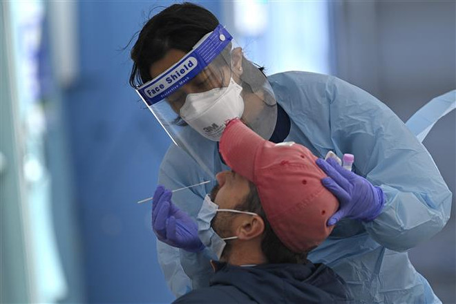 Nhân viên y tế lấy mẫu xét nghiệm COVID-19 cho người dân tại Sydney, Australia. (Ảnh: AFP/TTXVN) Australia mở cửa biên giới vào Giáng sinh, New Zealand hạ mức cảnh báo ảnh 1