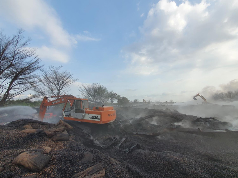 Hàng chục chiếc xe xúc đang cào lớp hạt điều đã cháy để lực lượng Phòng cháy chữa cháy và Cứu nạn, cứu hộ tiến hành làm mát kho hàng của Công ty cổ phần Thành Chí. (Ảnh: Huỳnh Ngọc Sơn/TTXVN)