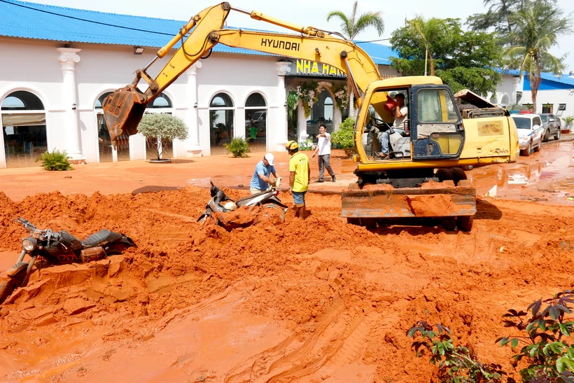 Người dân cùng tham gia cào cát và di chuyển xe máy bị vùi lấp ra ngoài. (Ảnh: Nguyễn Thanh/TTXVN)