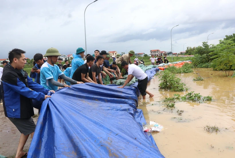 Người dân tích cực đắp cát, bạt qua đê để ngăn lũ. (Ảnh: Thanh Thương/TTXVN)