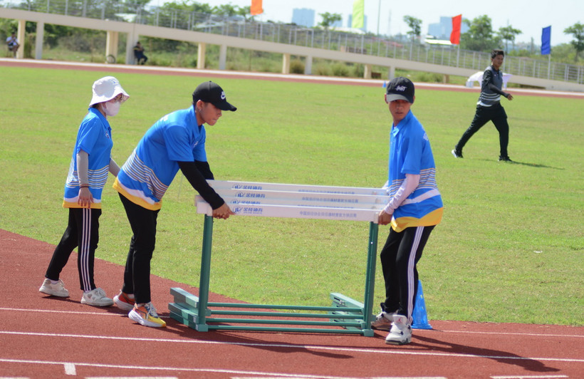 Tình nguyện viên hỗ trợ bố trí dụng cụ rào chắn vào sân thi đấu môn chạy vượt rào. (Ảnh: Văn Dũng/TTXVN)