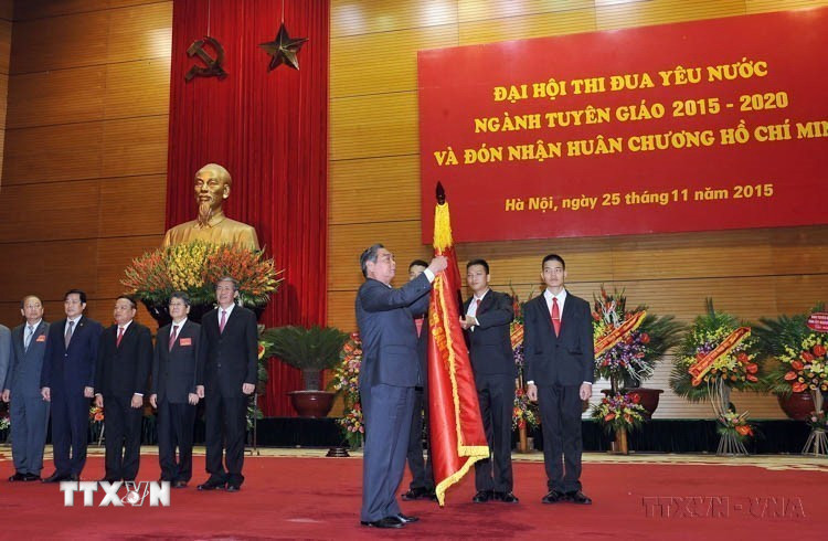 Thường trực Ban Bí thư Lê Hồng Anh gắn Huân chương Hồ Chí Minh lên lá cờ truyền thống ngành Tuyên giáo tại Đại hội Thi đua yêu nước ngành Tuyên giáo, giai đoạn 2015-2020 (25/11/2015). (Ảnh: Trọng Đức/TTXVN)