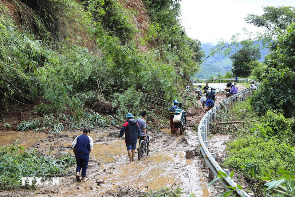 Người và xe máy vất vả di chuyển qua các điểm sạt lở. (Ảnh: TTXVN)