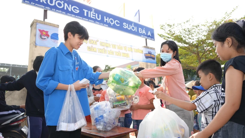 Đoàn viên Thanh niên xã Suối Đá thu gom chai nhựa sử dụng một lần và phát phiếu tham gia phiên chợ chai cho người dân. (Ảnh: Minh Phú/TTXVN)