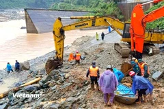 Phối hợp máy xúc và xuồng máy khẩn trương cứu hộ 2 người dân bị cô lập do nước lũ chia cắt. (Ảnh: PV/Vietnam+)