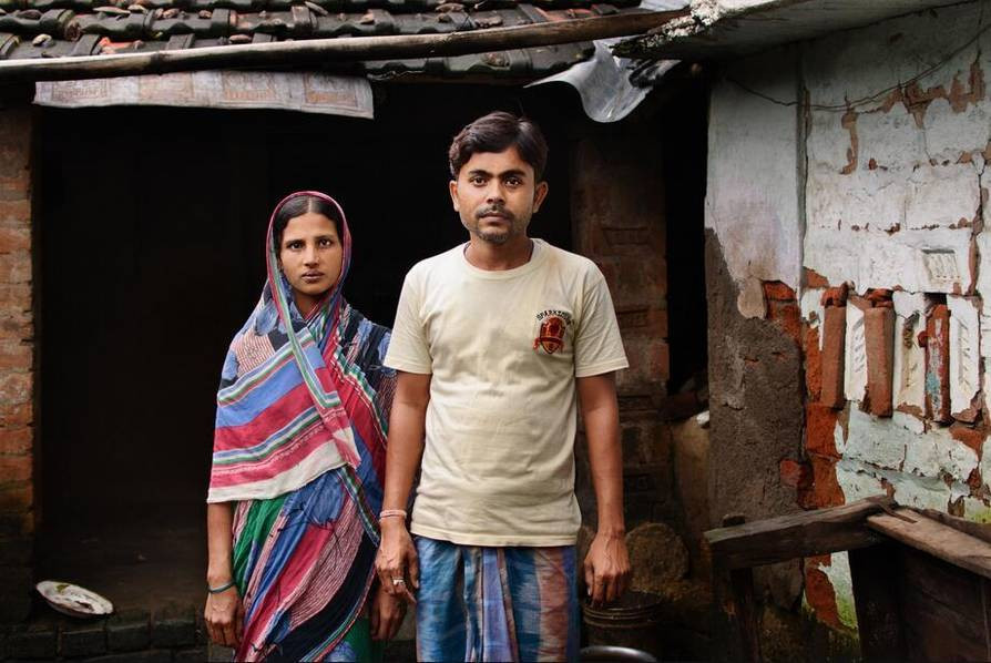 B và A đứng tại căn nhà của họ. Tháng Ba năm nay, cô con gái mới 6 tuổi của họ đã bị hàng xóm giết sau khi hiếp dâm. Thi thể của cô bé được tìm thấy trong một thửa ruộng gần đó. Trên người cô bé đầy vết thương, cánh tay bị gãy.