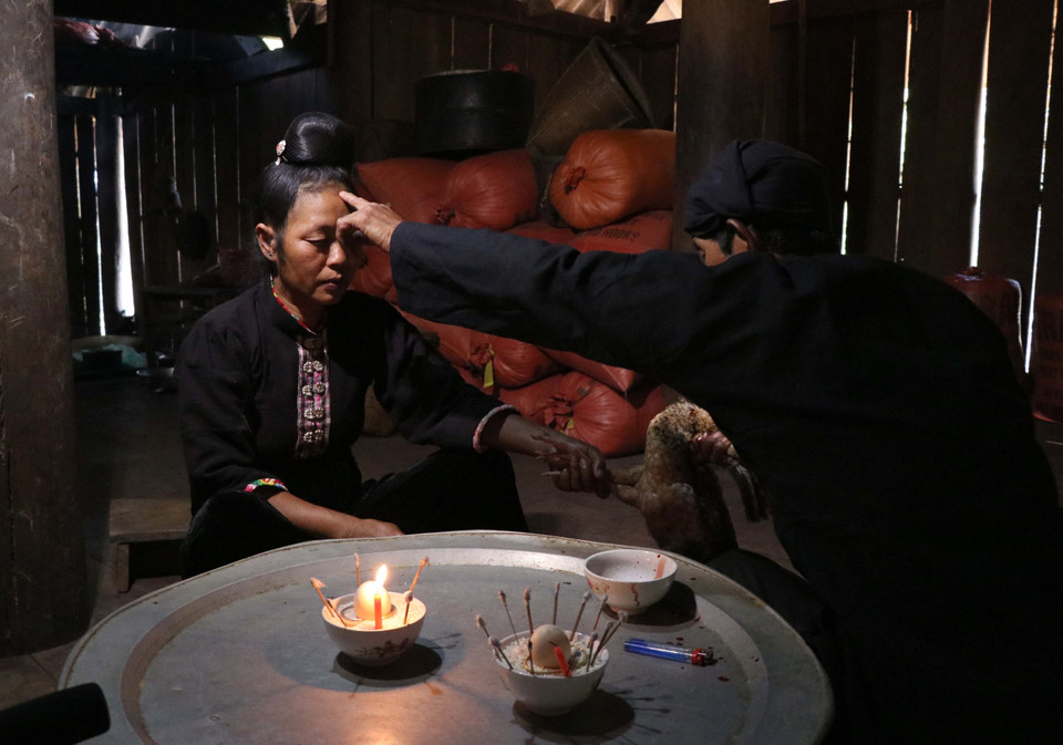 Thầy cúng lấy tiết gà đánh dấu lên trán cho gia chủ để cầu xin thần linh, tổ tiên phù hộ người trong gia đình gia chủ sang năm mới dồi dào sức khỏe, gặp nhiều điều an lành, may mắn. (Ảnh: Nguyễn Xuân Tiến/TTXVN)