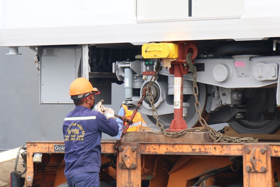Các kỹ sư, công nhân thực hiện công tác cố định toa xe lên xe vận chuyển. (Ảnh: Tiến Lực/TTXVN)