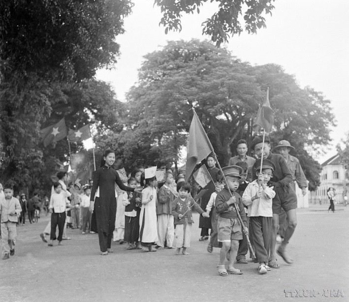 Thiếu nhi Hà Nội cùng người thân mang cờ chào đón bộ đội về giải phóng Thủ đô. (Ảnh: Tư liệu TTXVN)