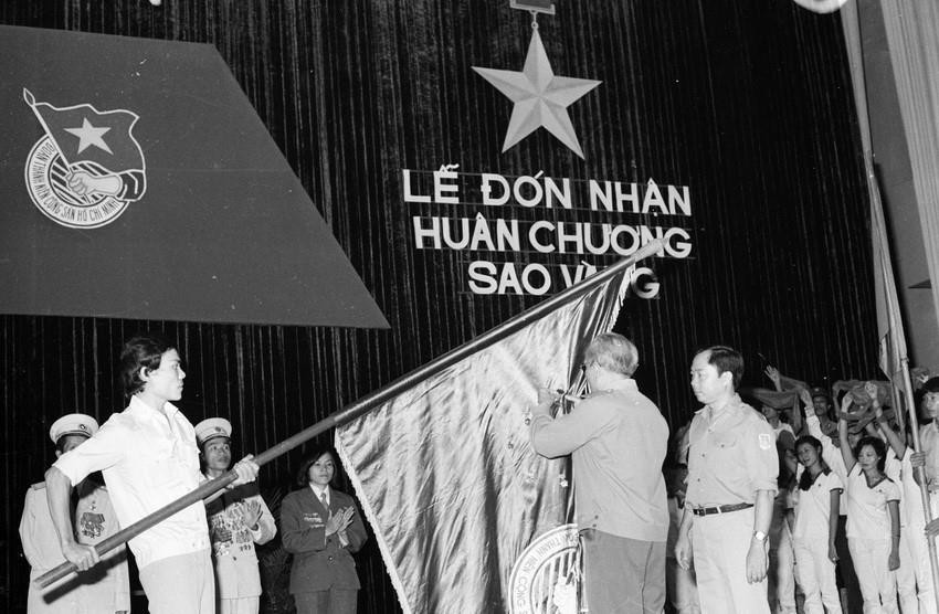 Đồng chí Chu Huy Mân gắn Huân chương Sao Vàng lên lá cờ truyền thống của Đoàn tại Lễ đón nhận Huân chương Sao Vàng do Hội đồng nhà nước trao tặng Trung ương Đoàn TNCS HCM (4/10/1985). (Ảnh: Minh Điền/TTXVN)