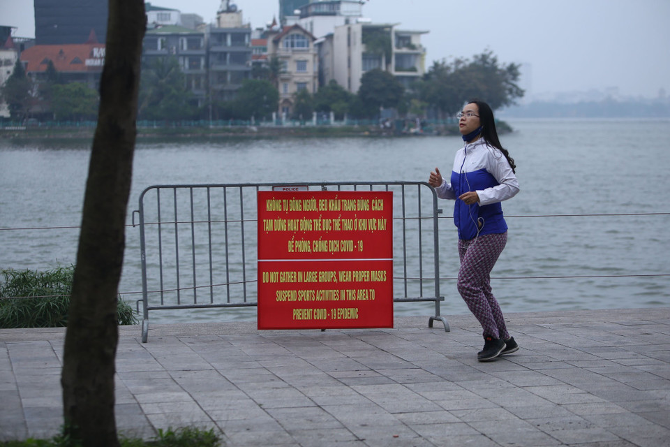 Nữ thanh niên đeo khẩu trang không đúng cách này tập thể dục ngay cạnh tấm biển khuyến cáo, nhắc nhở của chính quyền về phòng, chống dịch. (Ảnh: Anh Tuấn/TTXVN)