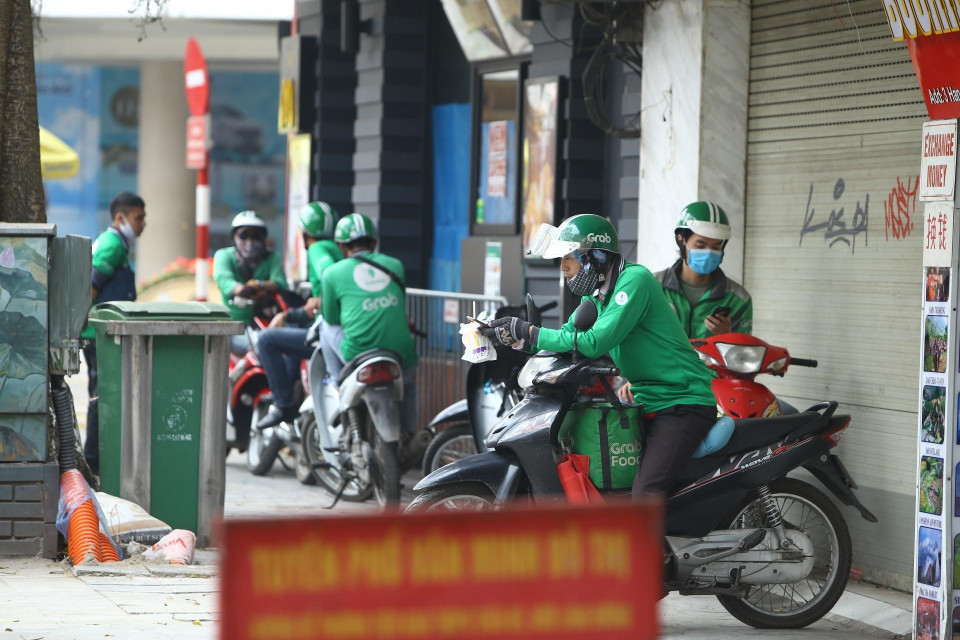 Các shipper tập trung đông trước cửa hàng chờ nhận đơn trên phố Hàng Khay (ảnh chụp trưa 21/4/2020). (Ảnh: Minh Quyết/TTXVN)