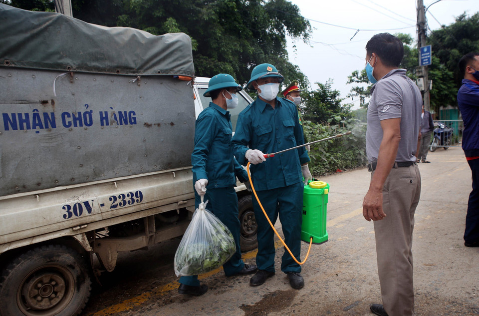 Phun thuốc khử khuẩn cho người và xe chở nhu yếu phẩm ra vào khu cách ly. (Ảnh: Danh Lam/TTXVN)