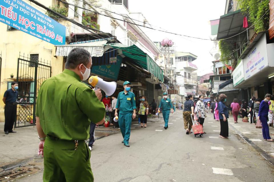 Lực lượng công an dùng loa phóng thanh nhắc nhở nhân dân giãn cách khi mua nhu yếu phẩm tại chợ Thanh Hà, phường Đồng Xuân, quận Hoàn Kiếm. (Ảnh: Doãn Tấn/TTXVN)