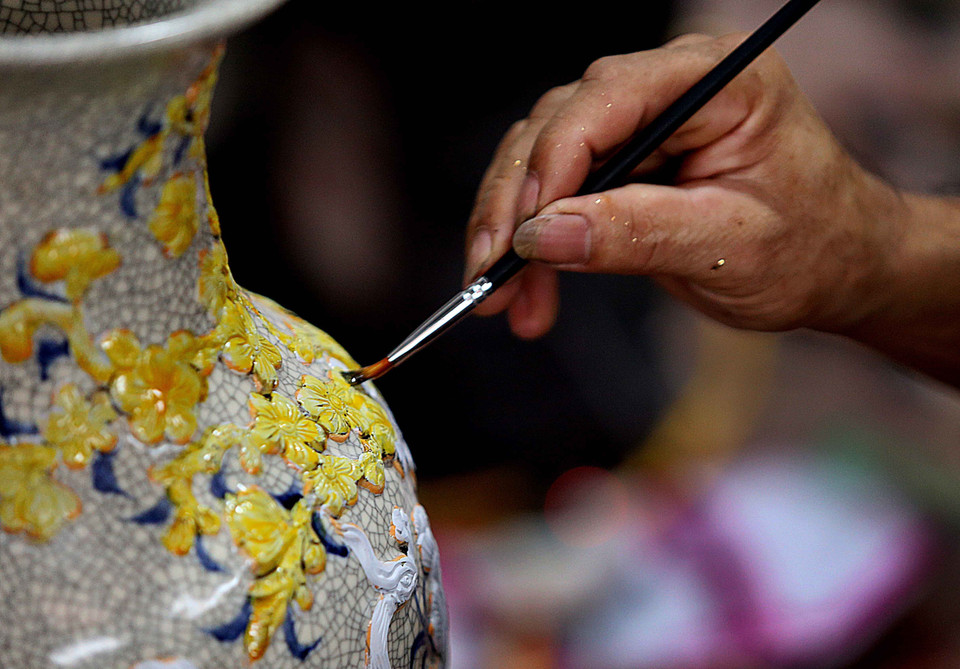 Bôi keo trước khi thiếp vàng trên sản phẩm sứ. (Ảnh: Hoàng Hiếu/ TTXVN)