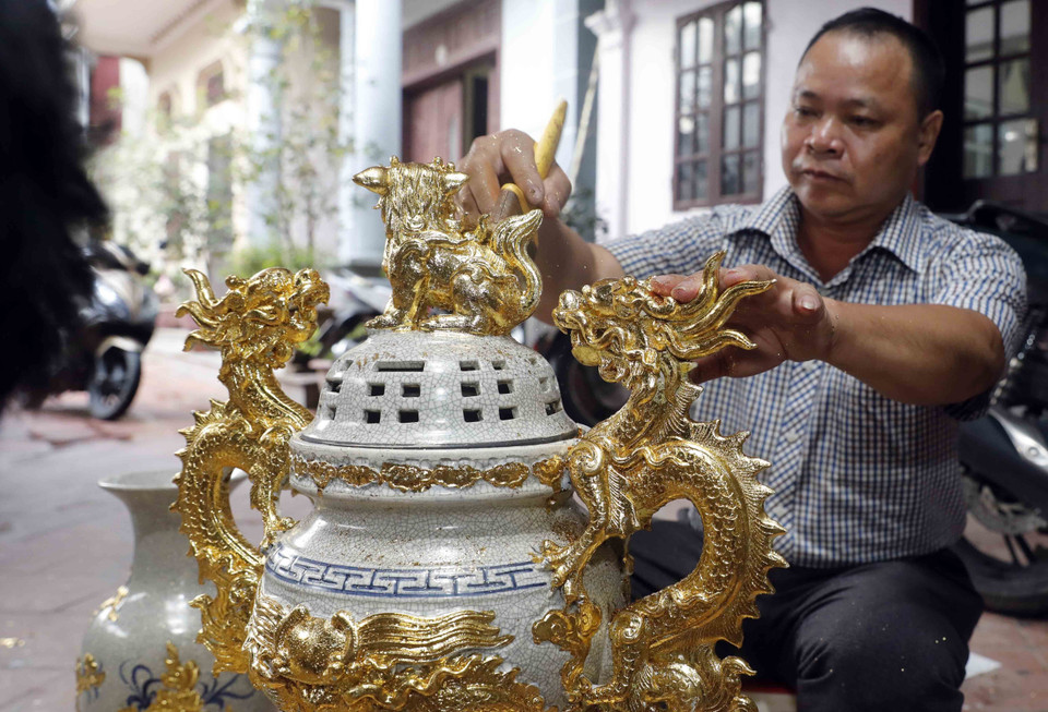 Nghệ nhân Nguyễn Anh Chung với sản phẩm dát vàng trên sứ. (Ảnh: Trần Việt/TTXVN)