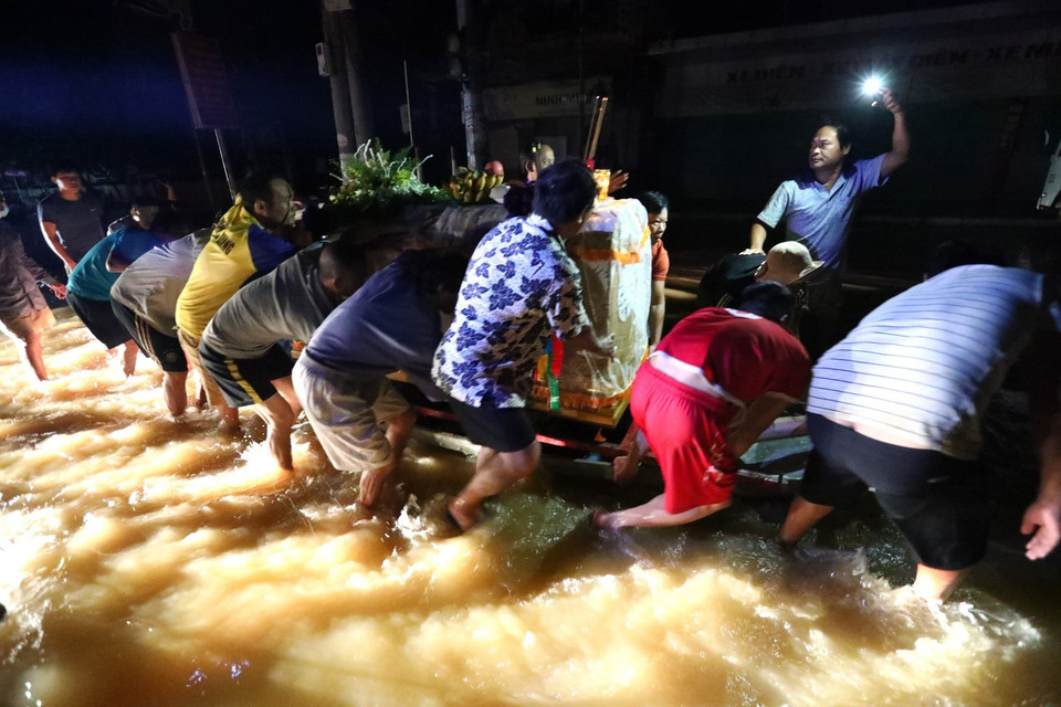 Người nhà vất vả di chuyển linh cữu trong đêm, xung quanh là nước lũ. (Ảnh: Thành Đạt/TTXVN)