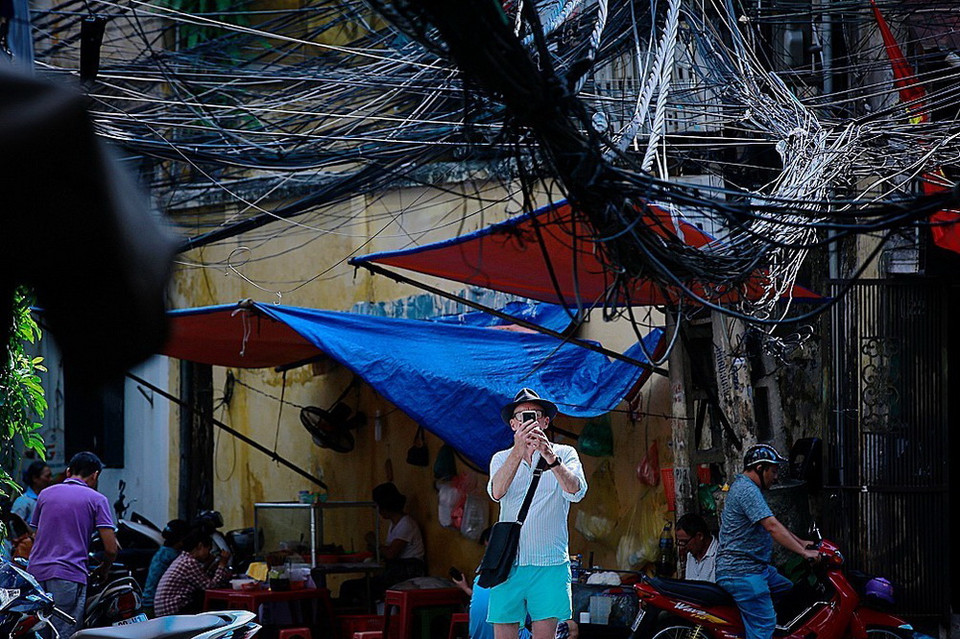 Một du khách hiếu kỳ dừng lại chụp lại hình ảnh các loại dây sà xuống đường ngay phía trên đầu người qua lại ở ngõ Hội Vũ. Có lẽ ông ta rất ngạc nhiên khi chứng kiến cảnh này. (Ảnh: Trọng Đạt/TTXVN)