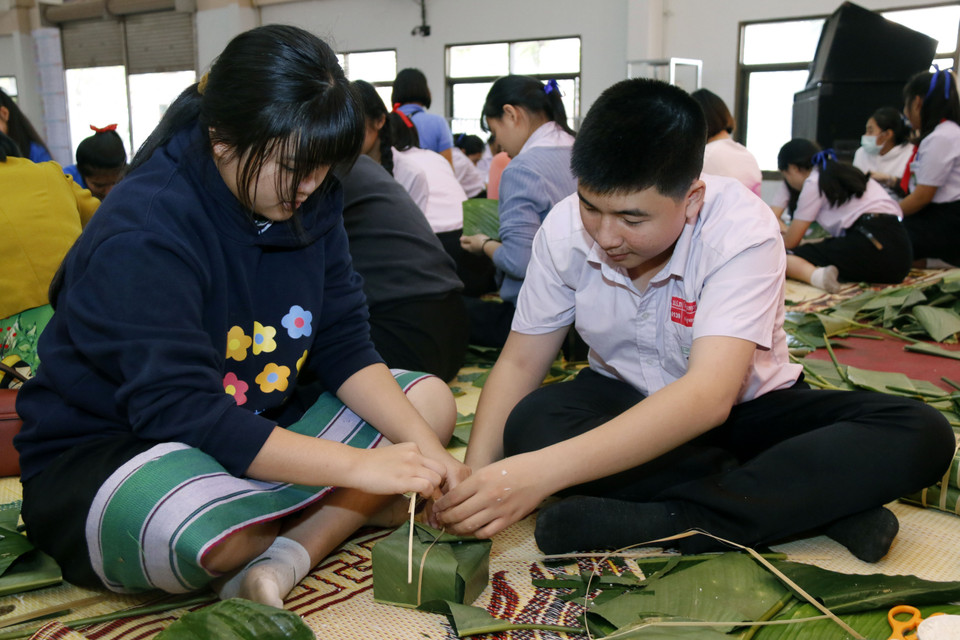 Em Trịnh Trọng Thái (phải), học sinh lớp 9 rất vui khi được hướng dẫn các bạn học Lào cách gói bánh chưng. (Ảnh: Phạm Kiên/Vietnam+)