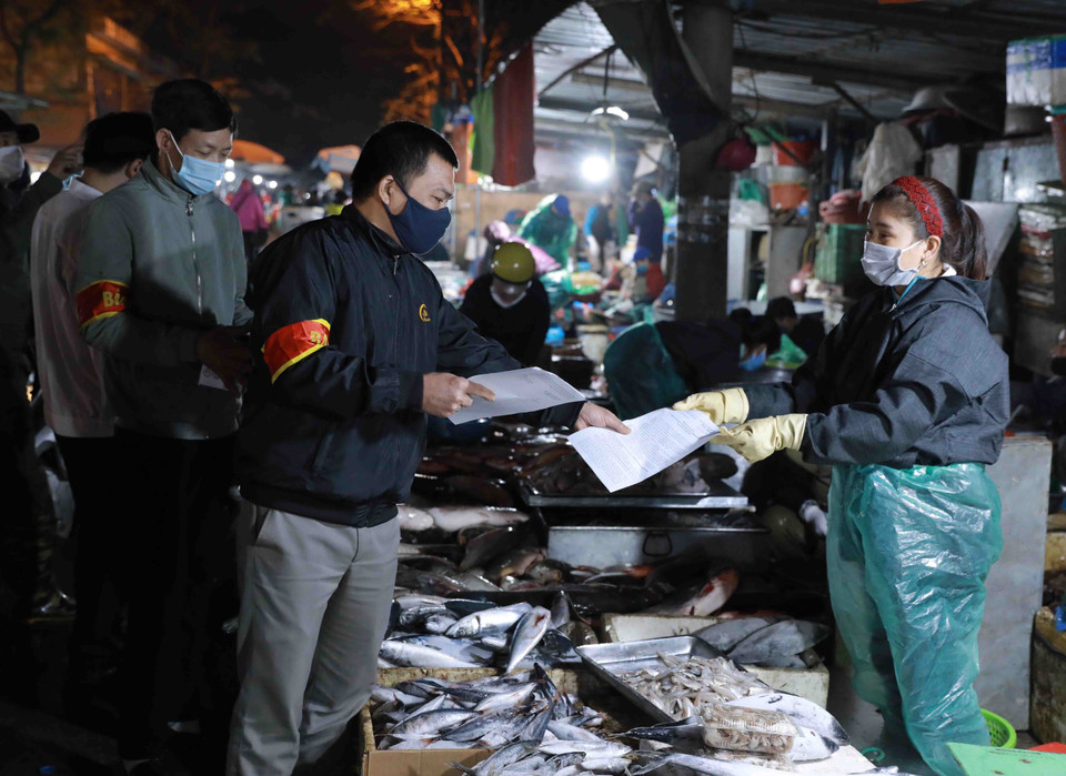 Nhân viên Ban Quản lý chợ phát khẩu trang y tế và tuyên truyền cho tiểu thương, người dân đến mua sắm nâng cao ý thức trong công tác phòng chống dịch bệnh. (Ảnh: Vũ Sinh/TTXVN)