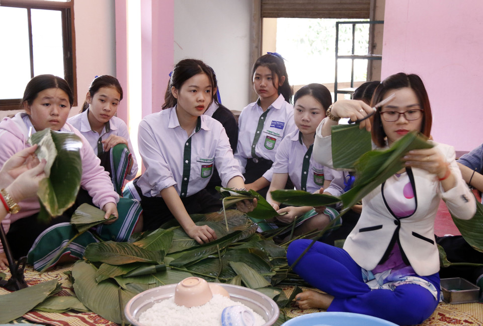 Các em học sinh chăm chú theo dõi các cô giáo hướng dẫn cách gói bánh. (Ảnh: Phạm Kiên/Vietnam+)