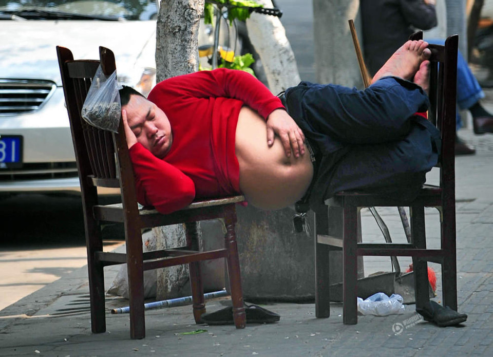 Người đàn ông béo nằm ngủ ngay trên vỉa hè với hai chiếc ghế. (Nguồn: QQ)
