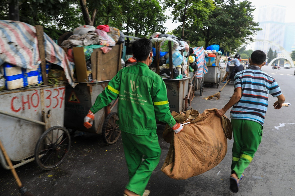 Công nhân môi trường vệ sinh, dọn rác thải vương vãi ra đường tại đường Khúc Thừa Dụ (quận Cầu Giấy). (Ảnh: Thành Đạt/TTXVN)