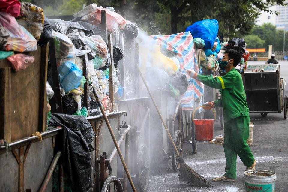 Chiều 3/11, tại đường Khúc Thừa Dụ công nhân môi trường phải căng bạt che rác và rắc vôi khử trùng vì không có điểm tập kết rác. (Ảnh: Thành Đạt/TTXVN)